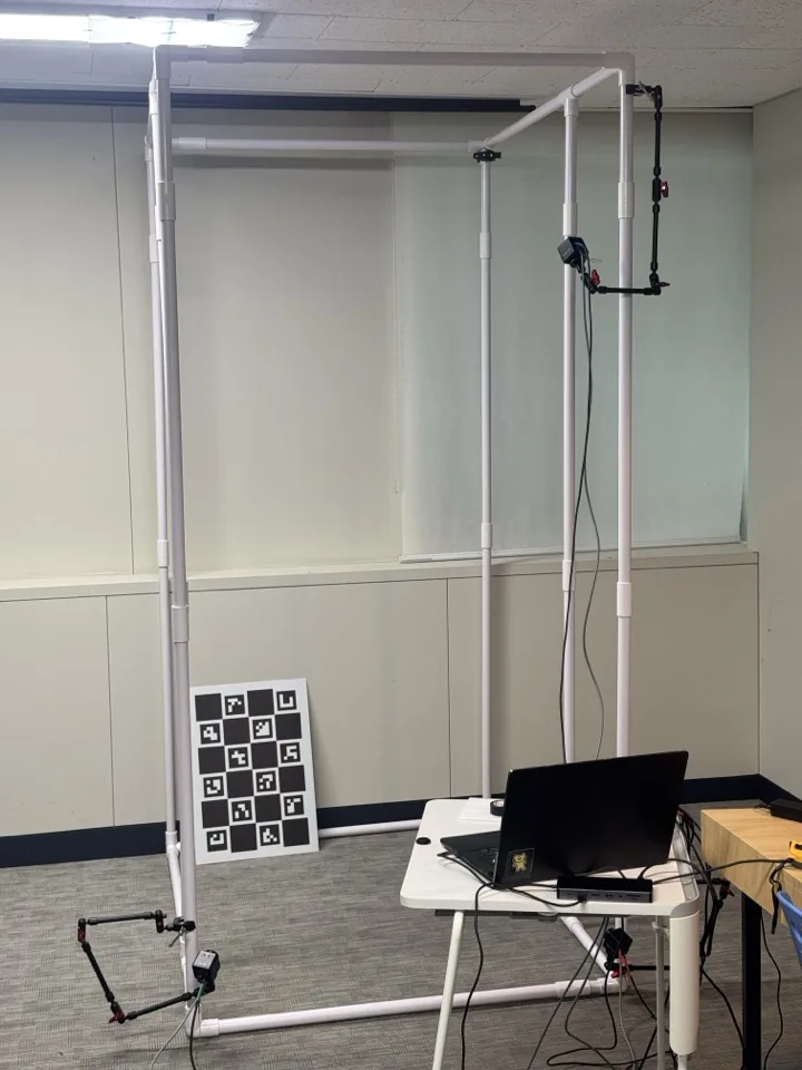 ChArUco calibration board leaning on the rig beside a laptop running the kiosk