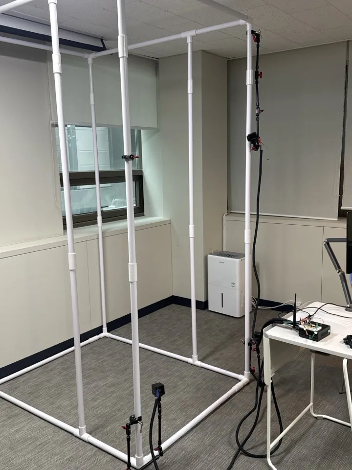 PVC power-rack mock-up in a lab room with three cameras clamped to the uprights and a tablet on the bench